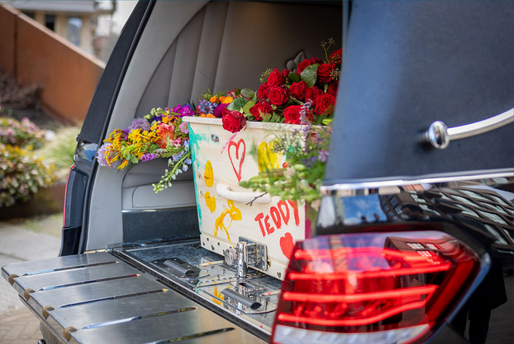 Een versierde kist in een rouwauto met rode rozen.
