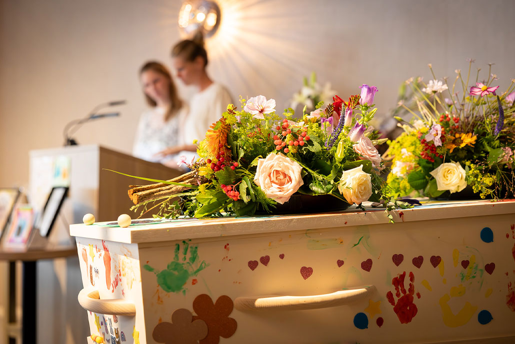 Dochters nemen afscheid van hun moeder. Een versierde kist met gekleurde bloemen.